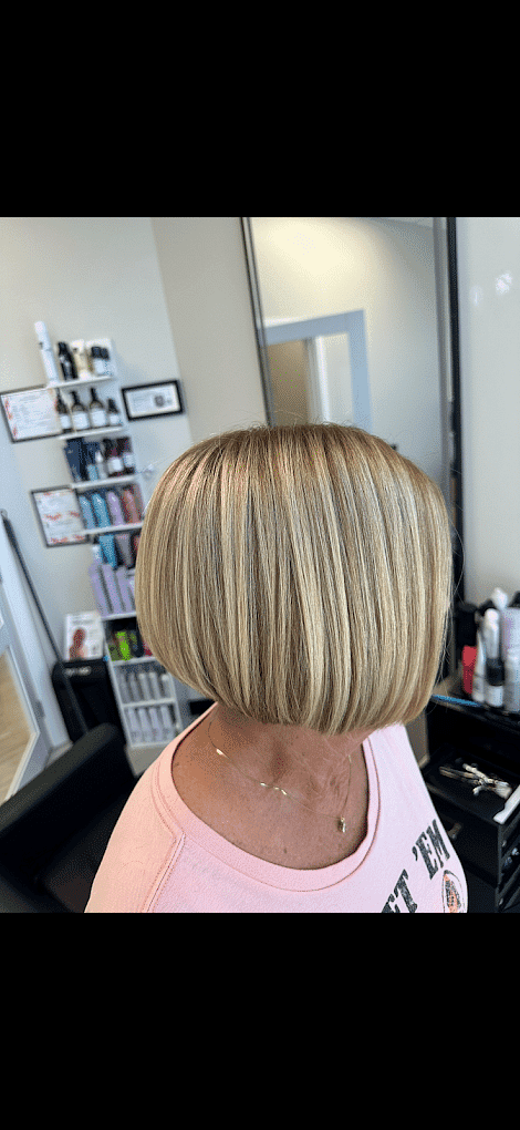 Woman with a blonde bob haircut in a salon, shelves of hair products in the background.